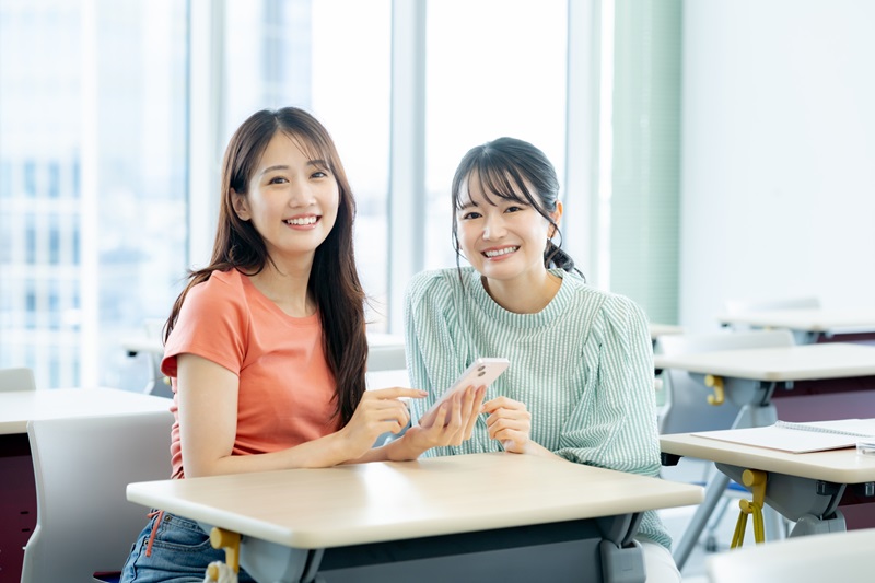 教室でスマホを見る女子大学生