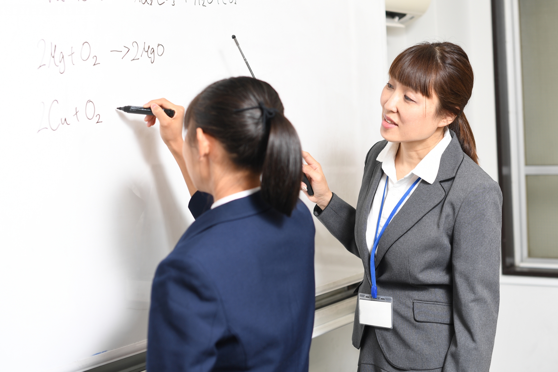 ホワイトボードに記入する女子学生と先生（講師）