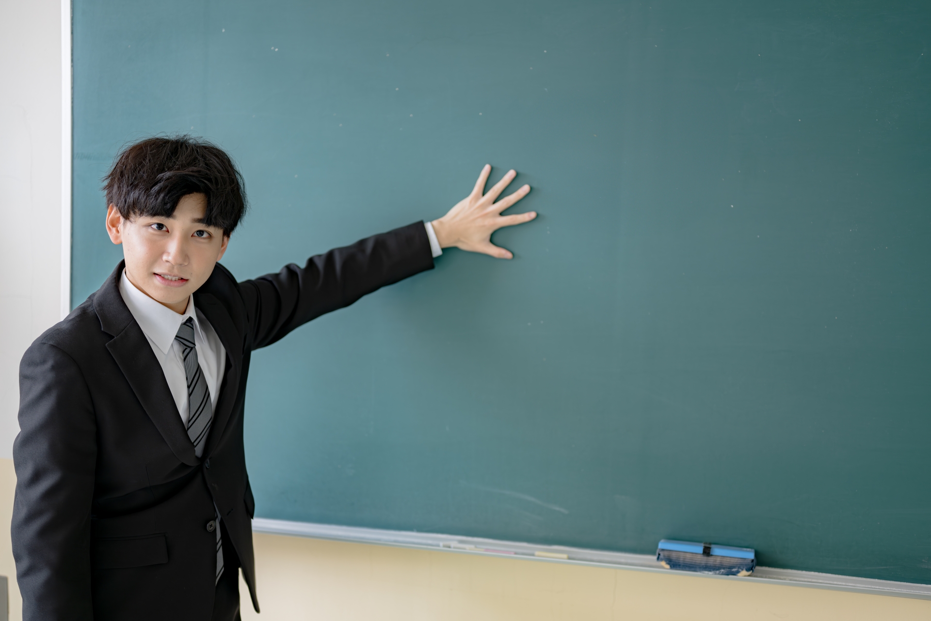 黒板に手を付くスーツの男性