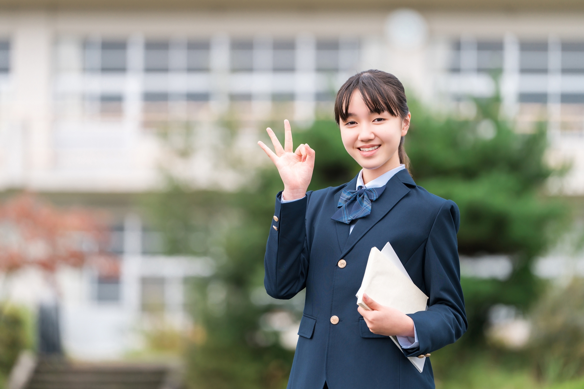 学校の校舎の前に立つ中学生・高校生