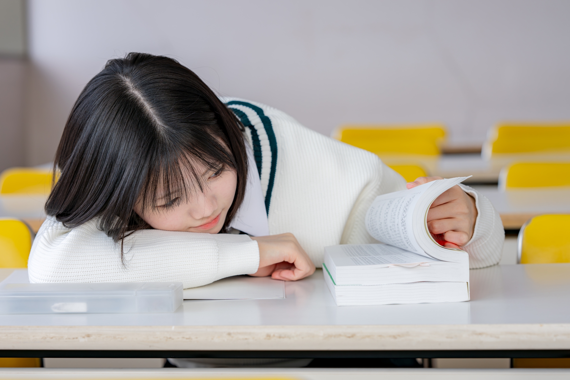 突っ伏しながら教科書を開く女子生徒